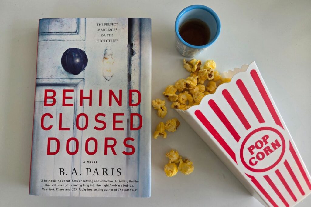 the book Behind Closed Doors with spilled popcorn and a shot of whiskey